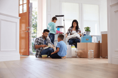 A family with two young children unpacking boxes in their new home, surrounded by moving supplies and open doors letting in natural light.